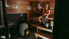 Mies istuu puusaunassa, HIVE Wood -kiuas näkyvissä